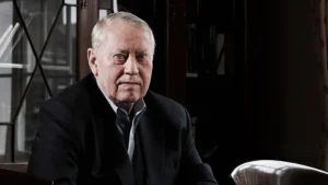 Portrait of Charles Feeney, an elderly man in a dark suit, seated in a library