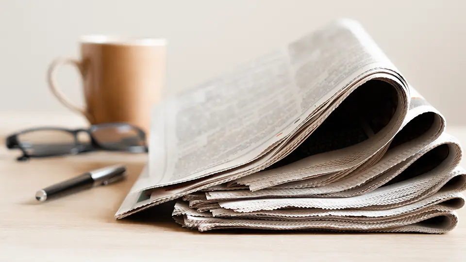Folded newspaper with coffee cup and glasses on desk — financial news and charitable giving insights blog