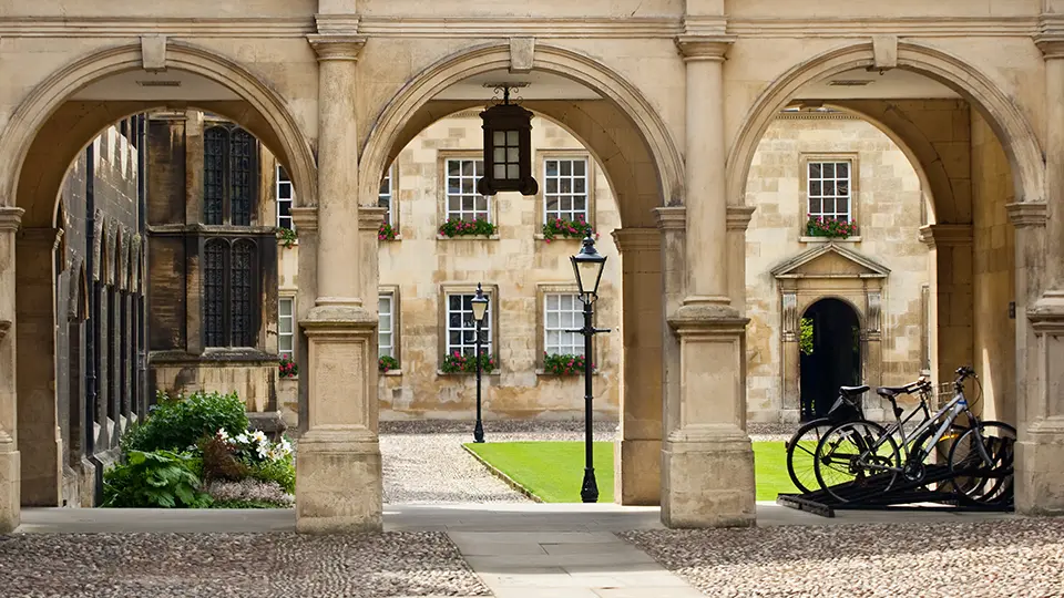 Brownstone arches in a historic university courtyard with bikes and flower-filled windows.