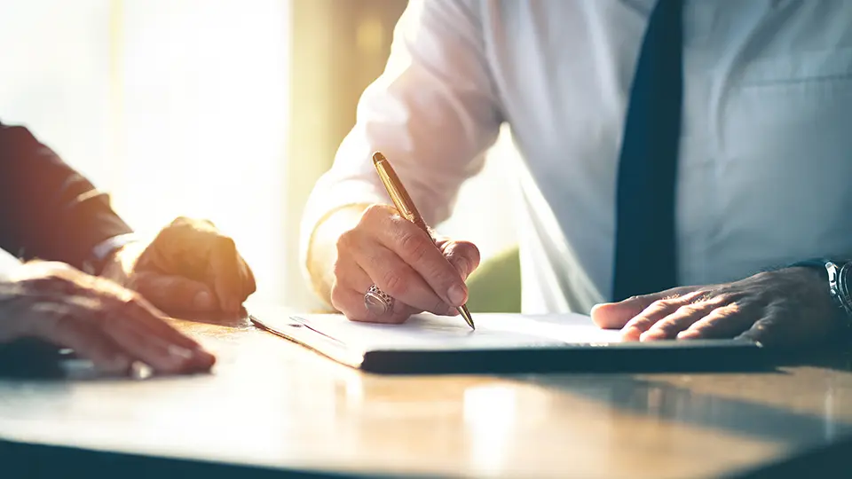 A businessman signing a contract at an office desk with a colleague