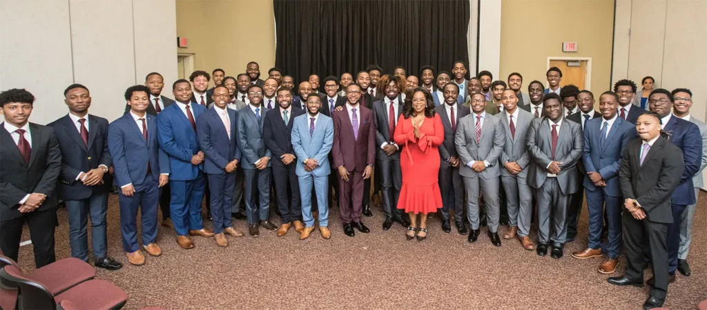 Large group of Morehouse College students in suits posing with Oprah Winfrey at campus event