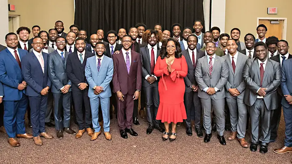 Large group of Morehouse College students in suits posing with Oprah Winfrey at campus event