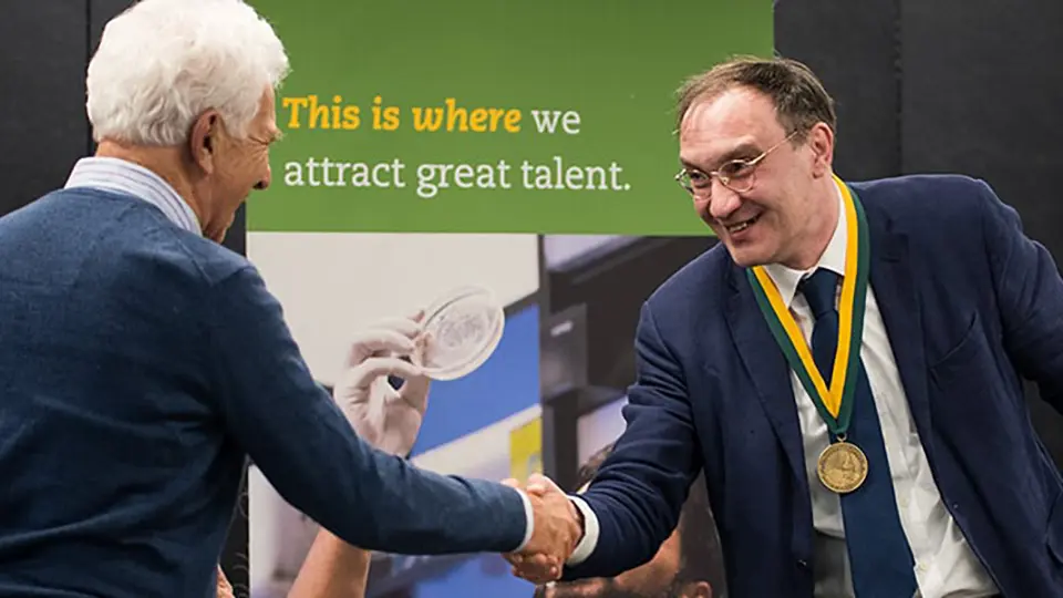 Andrey D. Ukhov, Ph.D., receiving recognition as the first Pizzagalli Chair of Free Enterprise, shaking hands during award ceremony with medal around his neck.