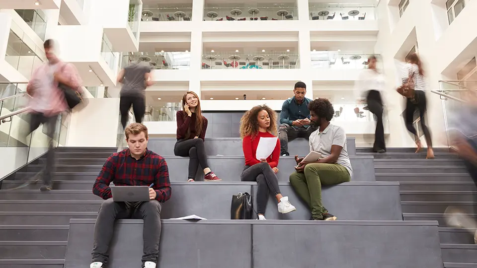 College students collaborating and studying together on campus steps inside a modern university building
