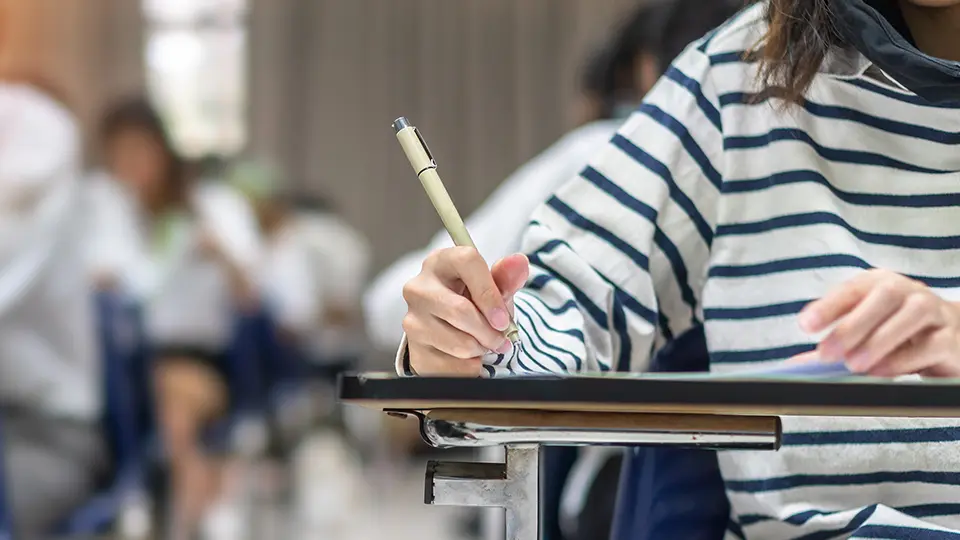 Students taking an exam in a classroom, writing on a test paper at a desk