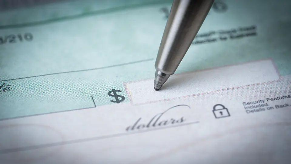 Close-up of a pen writing a dollar amount on a blank personal check, representing financial transactions or banking.
